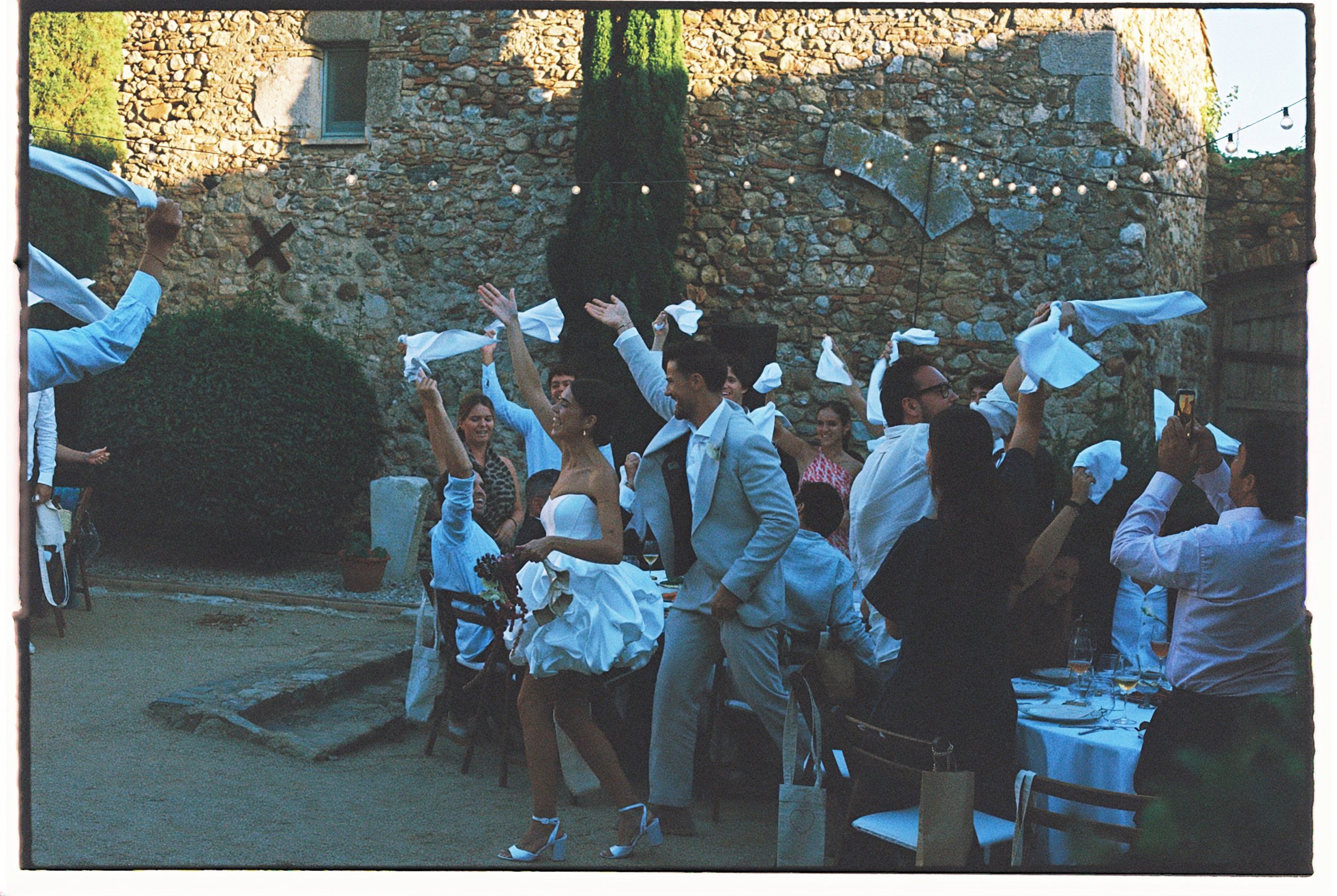 Invitados celebrando con servilletas al aire en un patio de piedra
