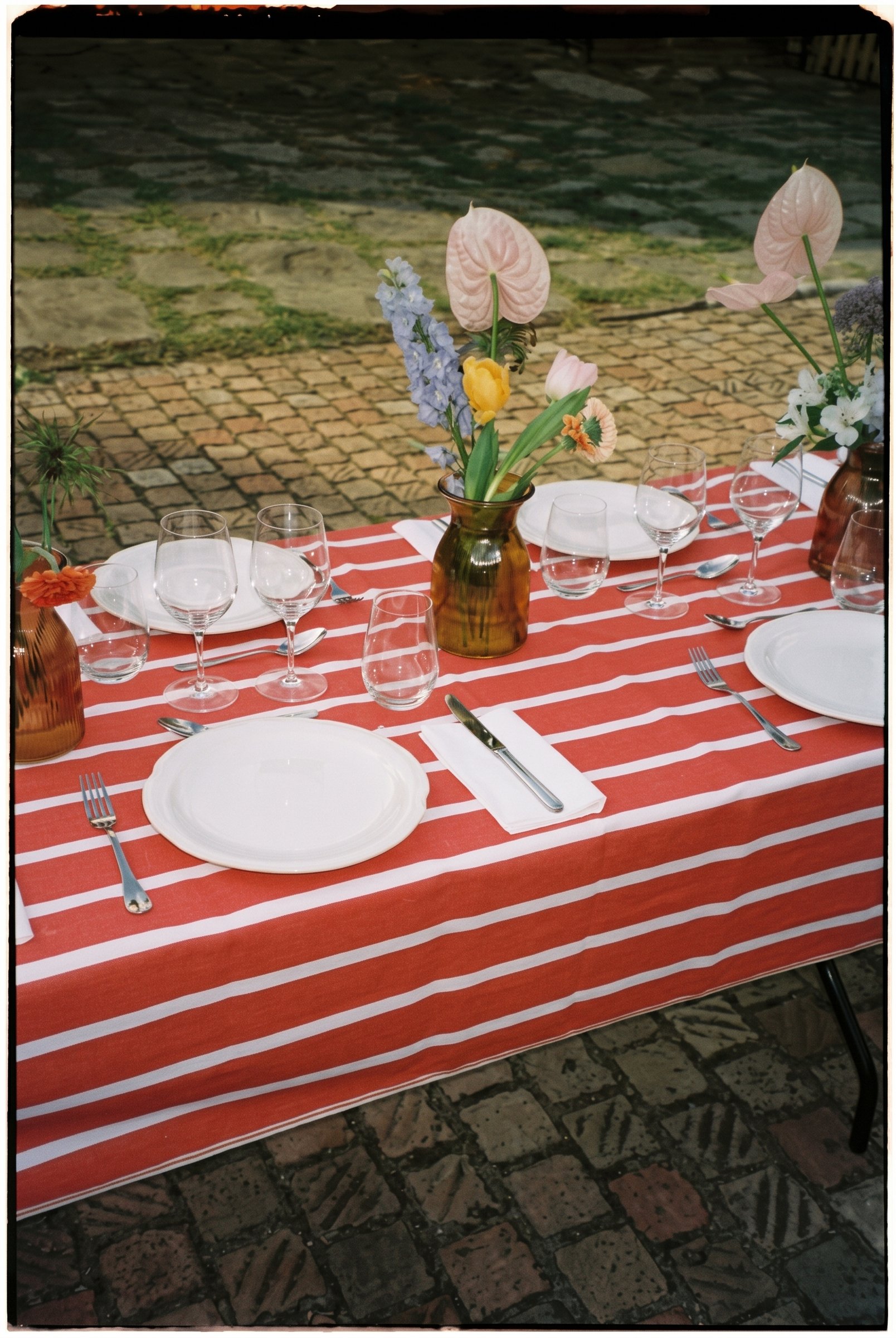 Mesa con mantel de rayas rojas y flores sobre el empedrado