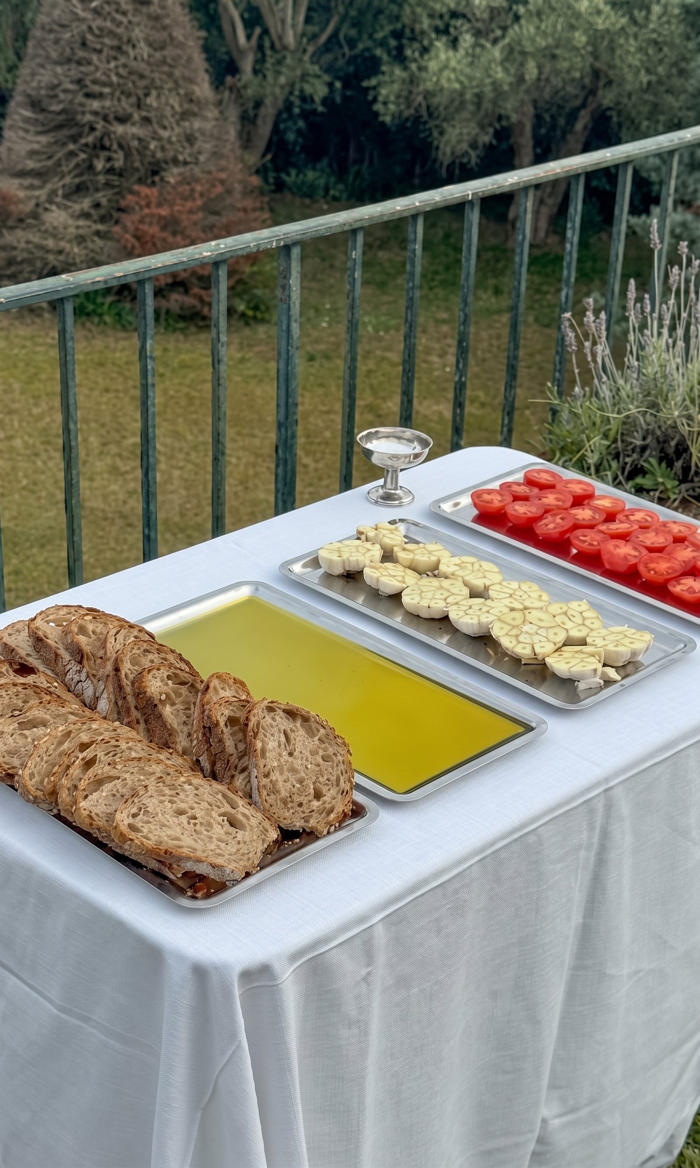 Pan, aceite, ajos y tomates en bandejas sobre una mesa en la terraza